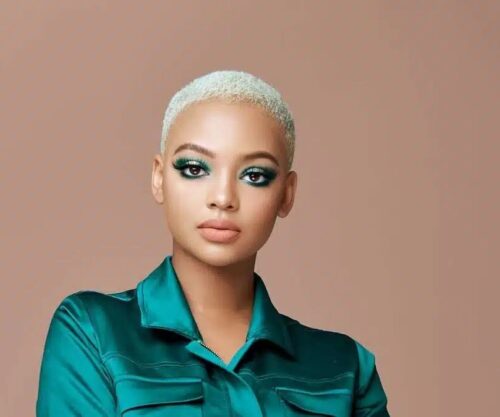 Mihlali Ndamase smiling by a BMW Gusheshe, social media influencer in vibrant street style, viral video reaction South Africa, Johannesburg vibe, Bona Magazine