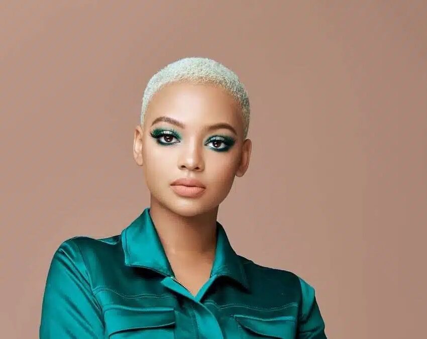 Mihlali Ndamase smiling by a BMW Gusheshe, social media influencer in vibrant street style, viral video reaction South Africa, Johannesburg vibe, Bona Magazine