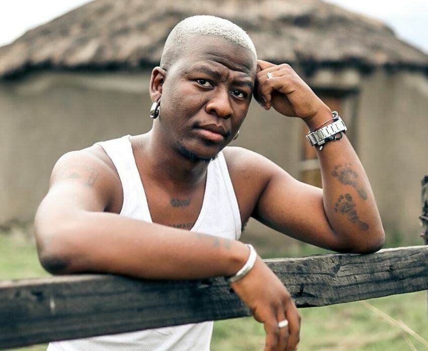 Bravo Le Roux portrait, South African hip hop artist, Khayelitsha musician, cultural ambassador, musician performing live, heartfelt tribute scene, social media reactions, celebrity memorial gathering, GoFundMe campaign graphic, Cape Town music event tribute, musician with family, emotional fan crowd, music community mourning Bona Magazine