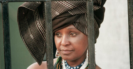 Winnie Mandela, the wife of political prisoner Nelson Mandela, looks out from behind the barred gate at her home, where she lived in defiance of a 1985 government order banishing her to the Orange Free State. (Photo by David Turnley/Corbis/VCG via Getty Images)
