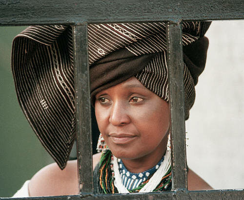 Winnie Mandela, the wife of political prisoner Nelson Mandela, looks out from behind the barred gate at her home, where she lived in defiance of a 1985 government order banishing her to the Orange Free State. (Photo by David Turnley/Corbis/VCG via Getty Images)