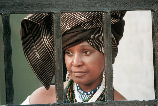 Winnie Mandela, the wife of political prisoner Nelson Mandela, looks out from behind the barred gate at her home, where she lived in defiance of a 1985 government order banishing her to the Orange Free State. (Photo by David Turnley/Corbis/VCG via Getty Images)