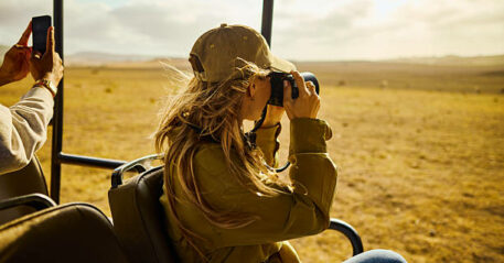 Young adult woman photographing wildlife from safari vehicle on african savanna