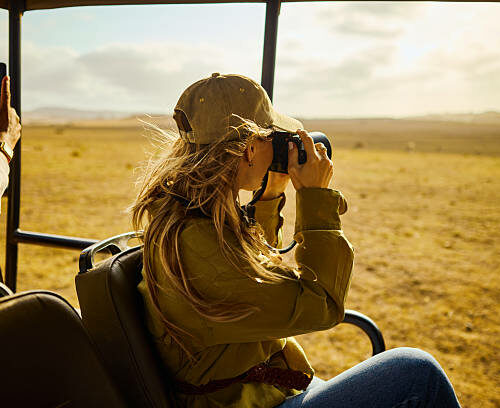 Young adult woman photographing wildlife from safari vehicle on african savanna