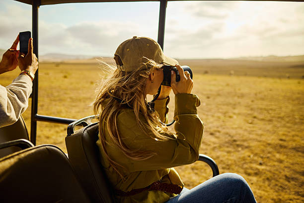 Young adult woman photographing wildlife from safari vehicle on african savanna